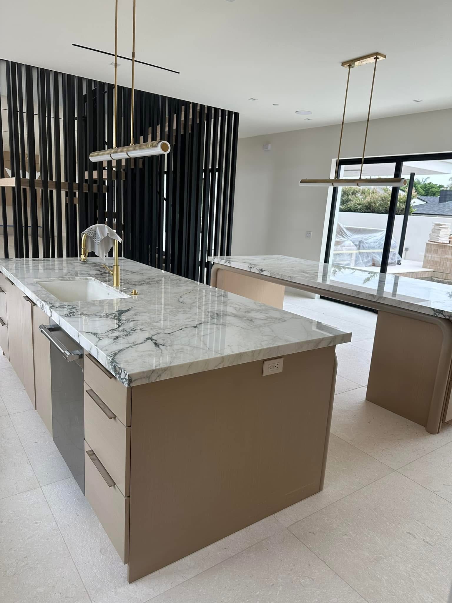 Modern kitchen with marble countertops, beige cabinetry, black slat wall feature, and brass pendant lighting