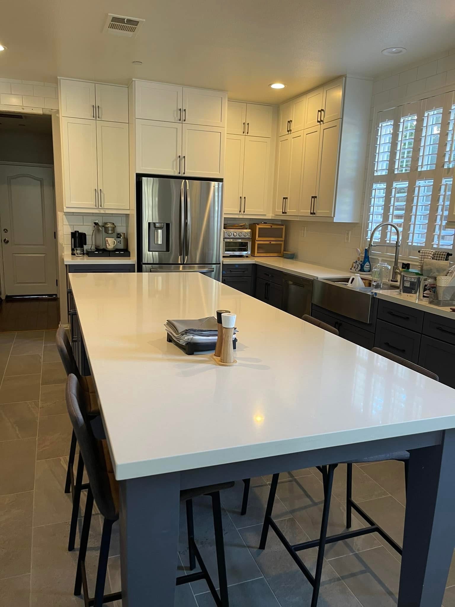 Modern kitchen with white upper cabinets, black lower cabinets, stainless steel refrigerator, white island with seating, and tile flooring