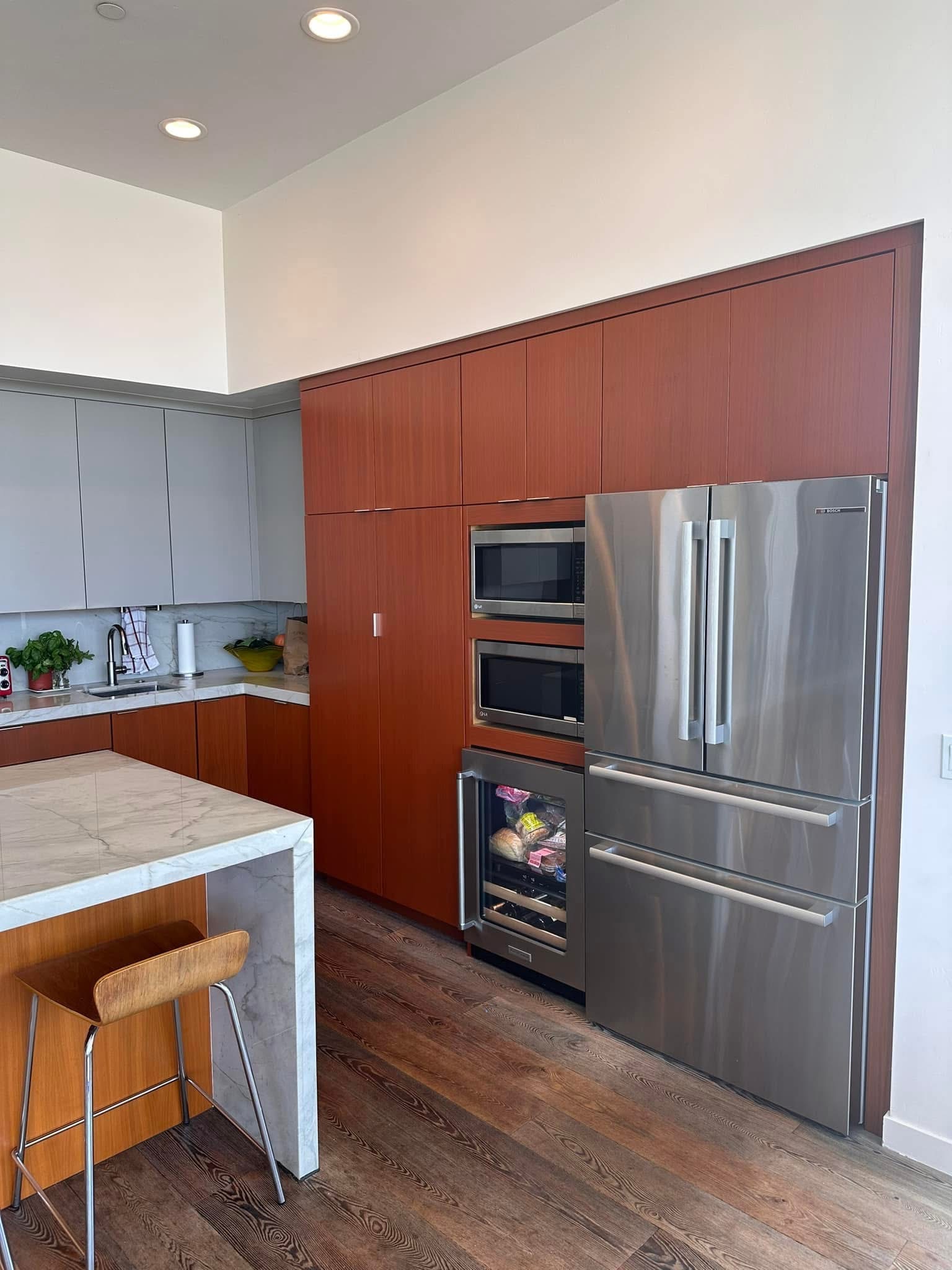Modern kitchen with red wood cabinetry, stainless steel appliances, and marble island with seating