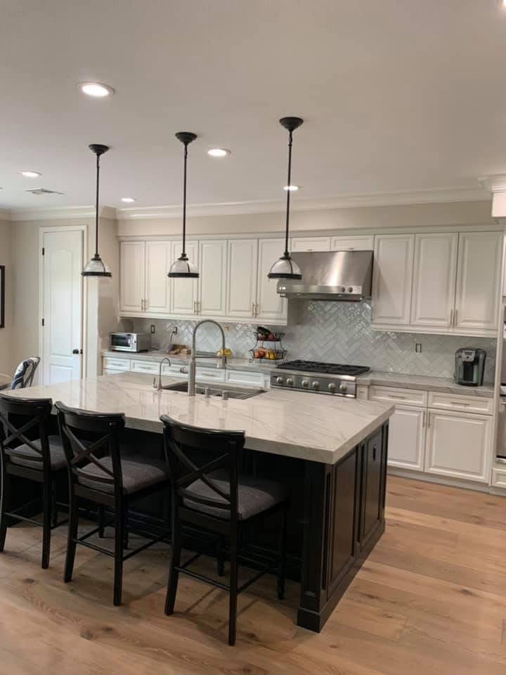 Modern kitchen with white cabinetry, black island, pendant lights, and marble countertops