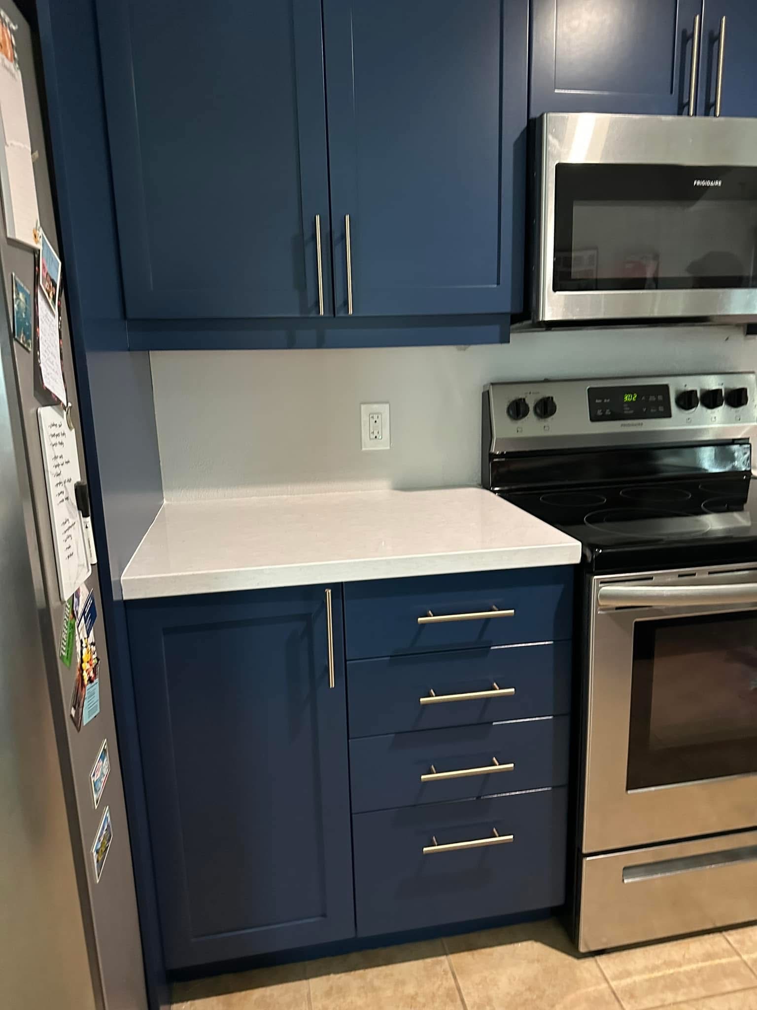 Modern kitchen with navy blue cabinets, white countertop, and stainless steel appliances