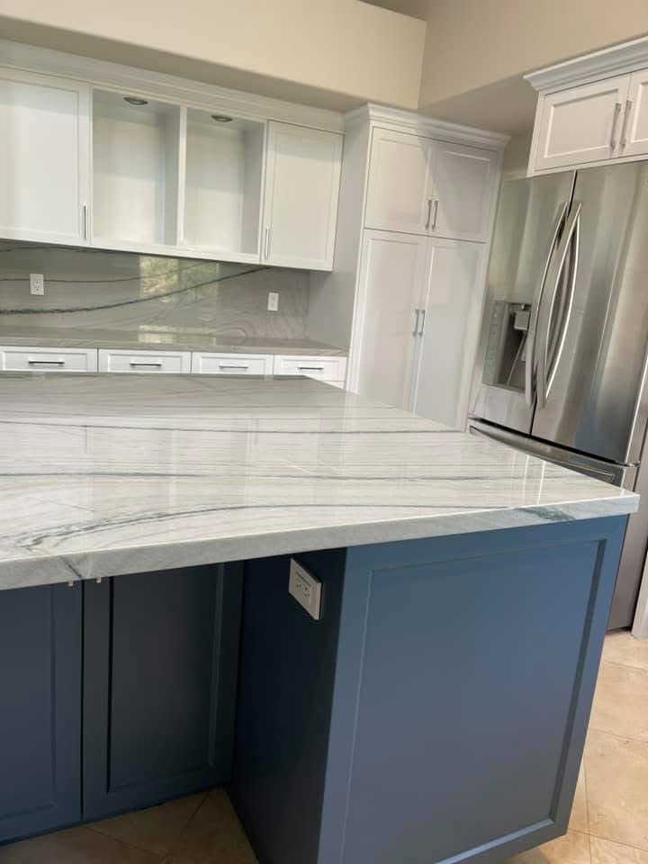 Modern kitchen with white cabinets, blue island, marble countertops and stainless steel appliances