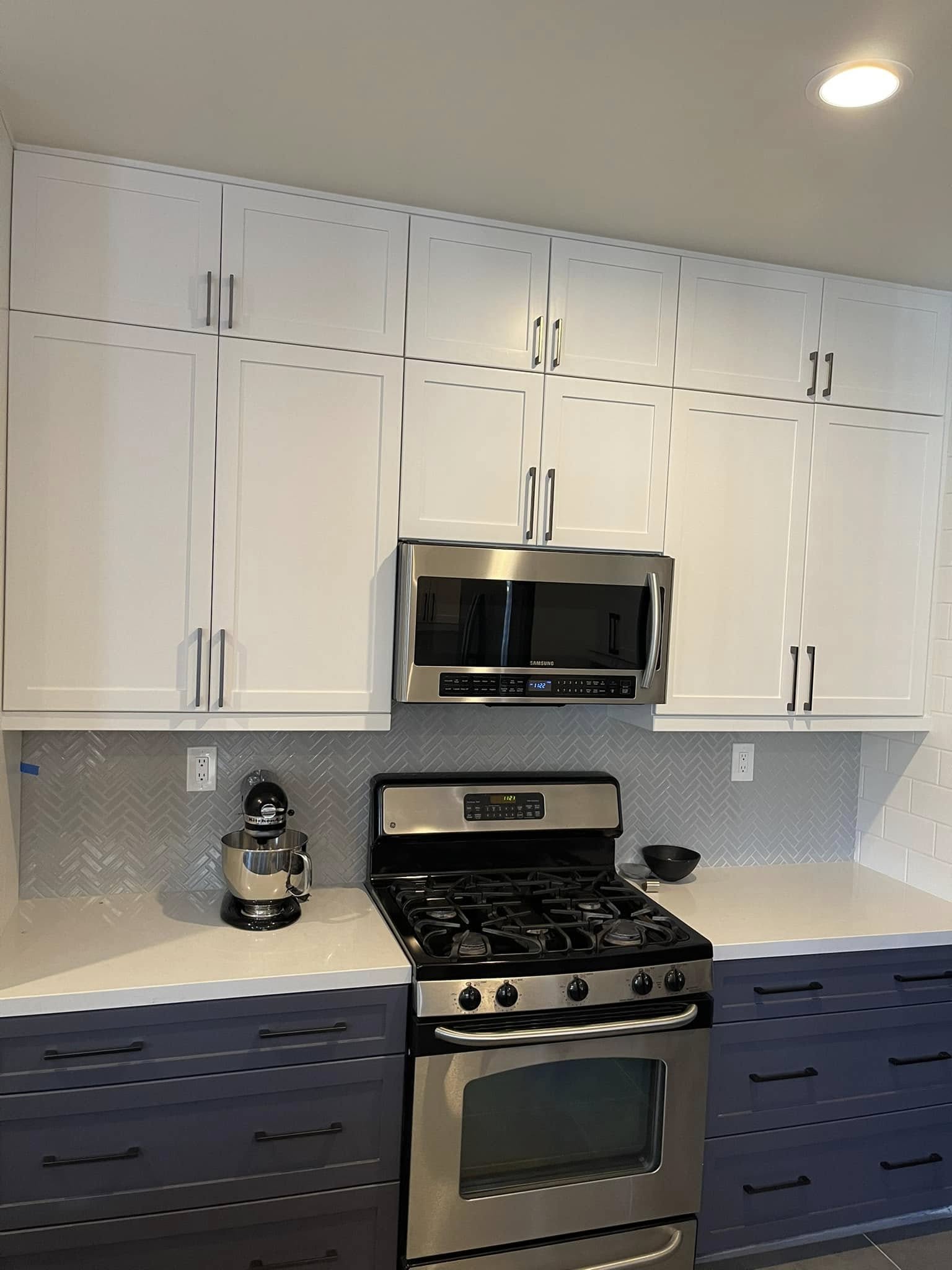 Modern kitchen with white upper cabinets, navy lower cabinets, stainless steel gas range and microwave, herringbone tile backsplash