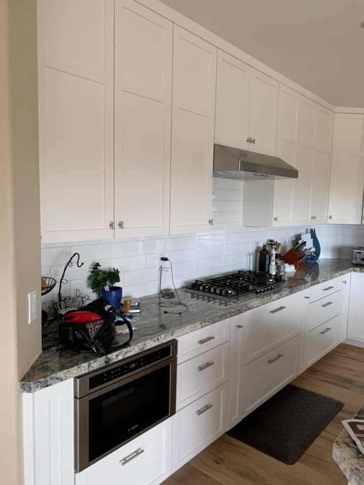 Modern white kitchen with granite countertops, stainless steel appliances and subway tile backsplash