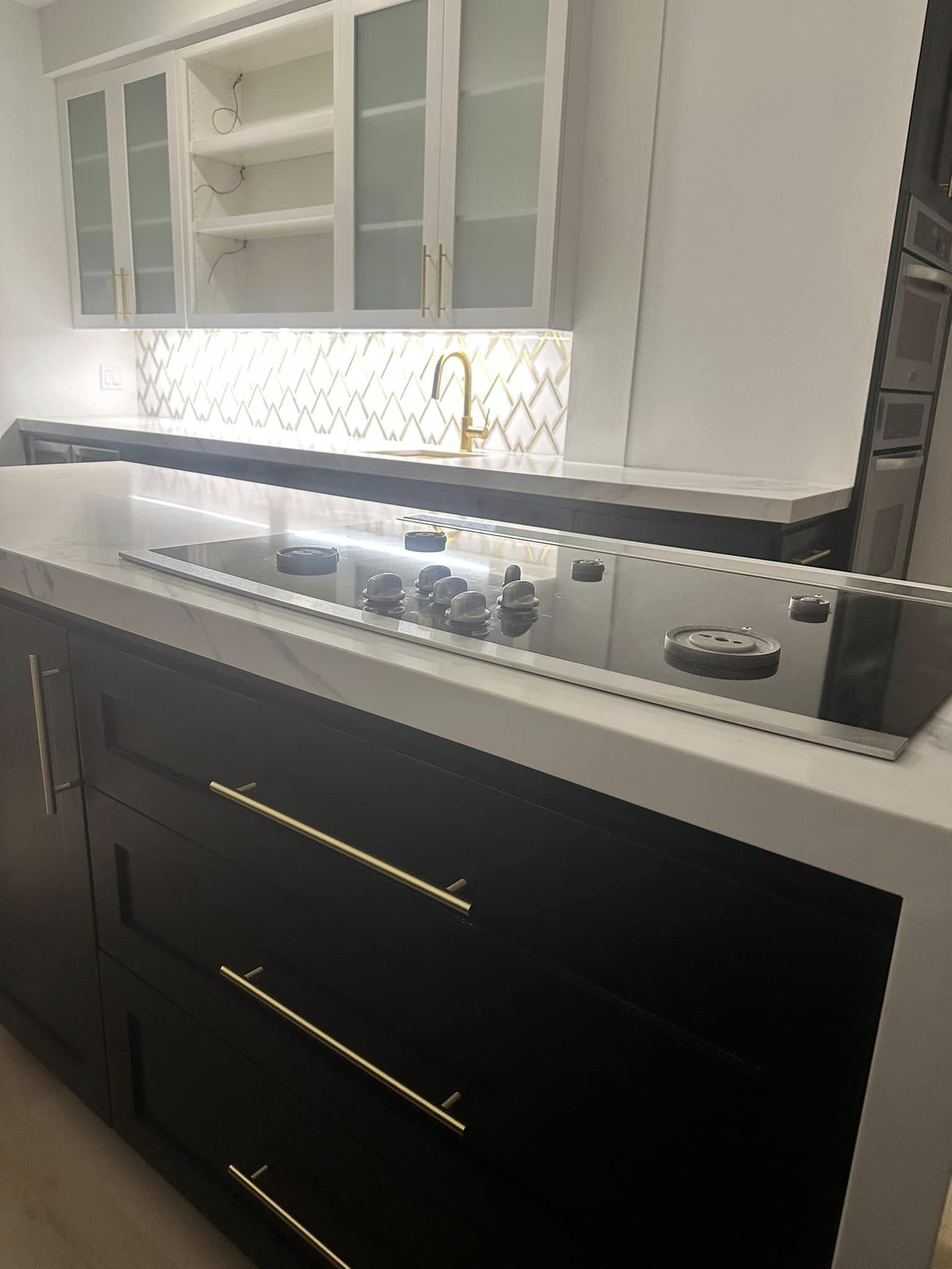 Modern kitchen with black cabinetry, white countertop, gas cooktop, and white upper cabinets with glass doors