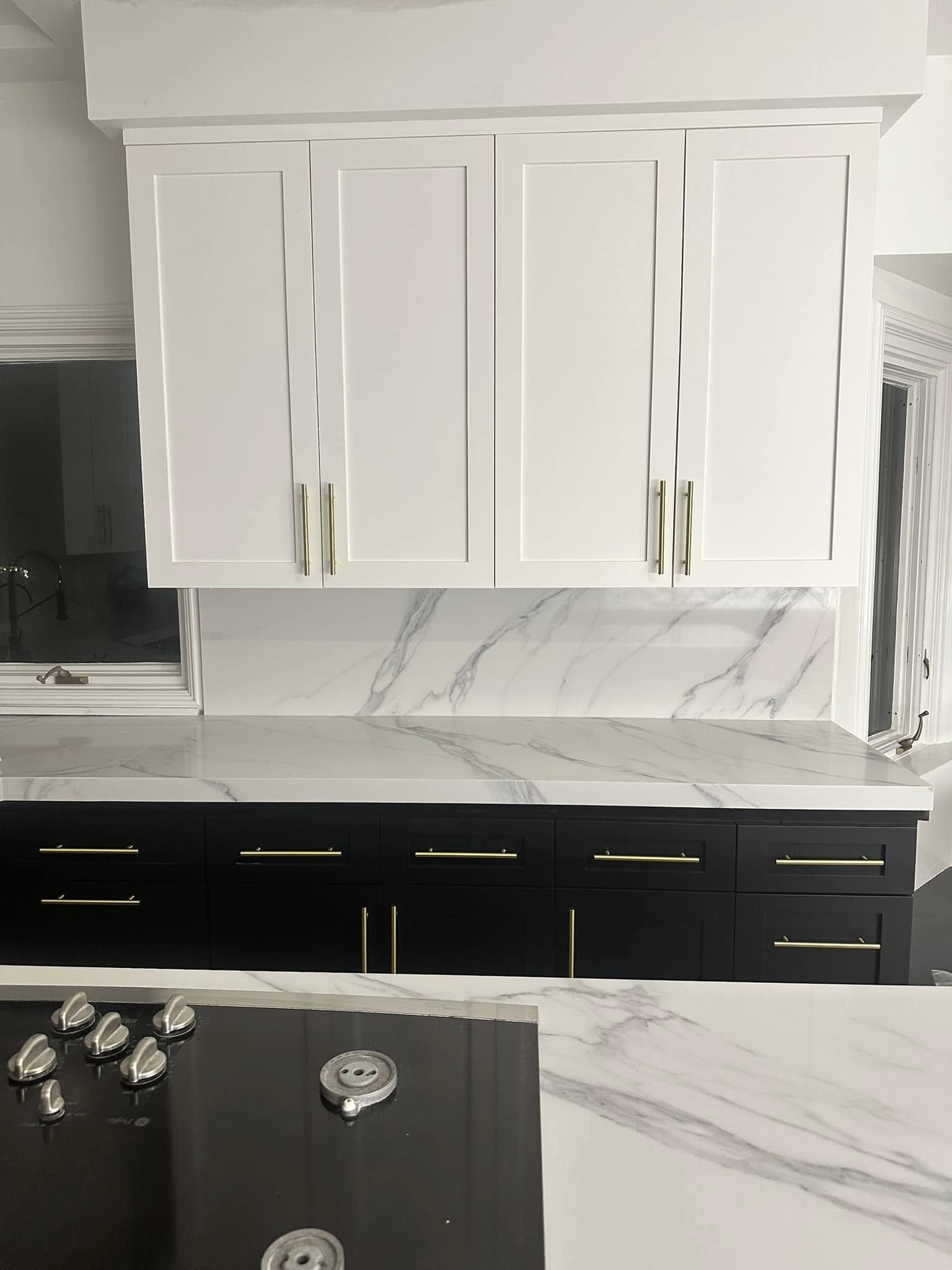 Modern kitchen with white upper cabinets, black lower cabinets, marble countertops and backsplash, gold hardware