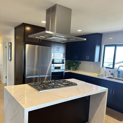 Modern kitchen with white marble island, gas cooktop, stainless steel appliances and navy blue cabinetry