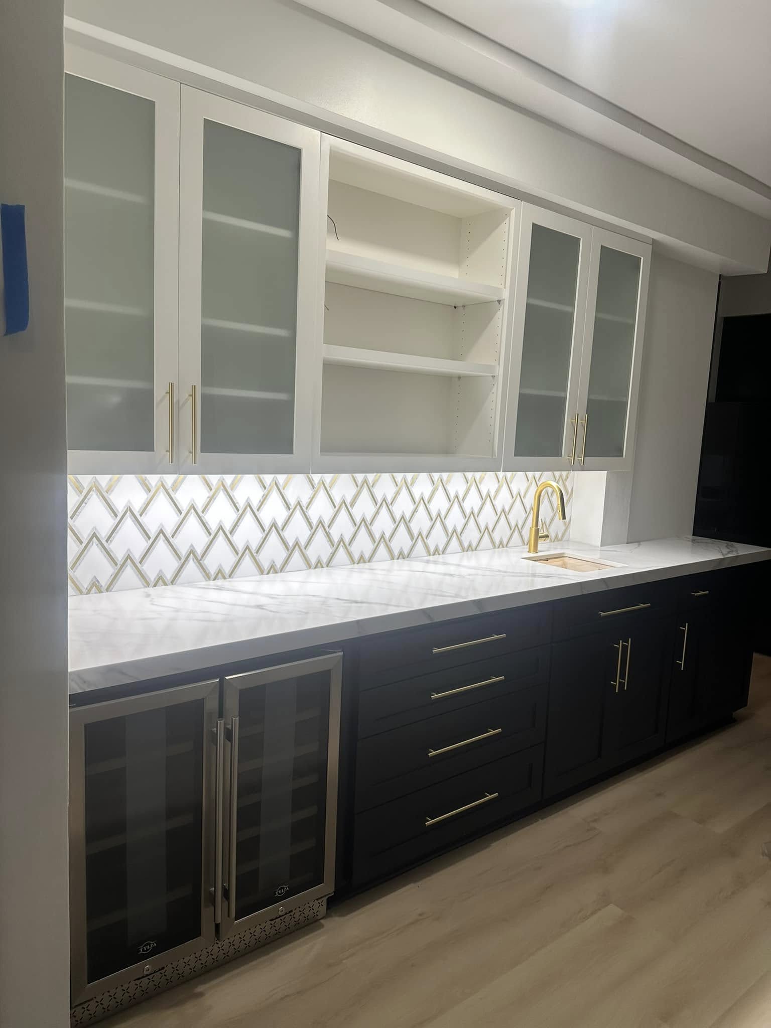 Modern kitchen with white upper cabinets, black lower cabinets, marble countertop, and geometric tile backsplash