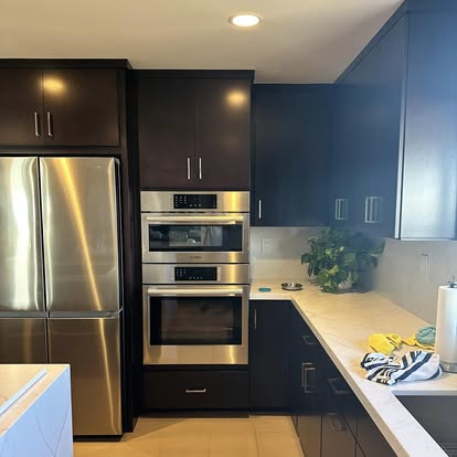 Modern kitchen with black cabinets, stainless steel appliances, blue upper cabinets, white countertop, and tile flooring