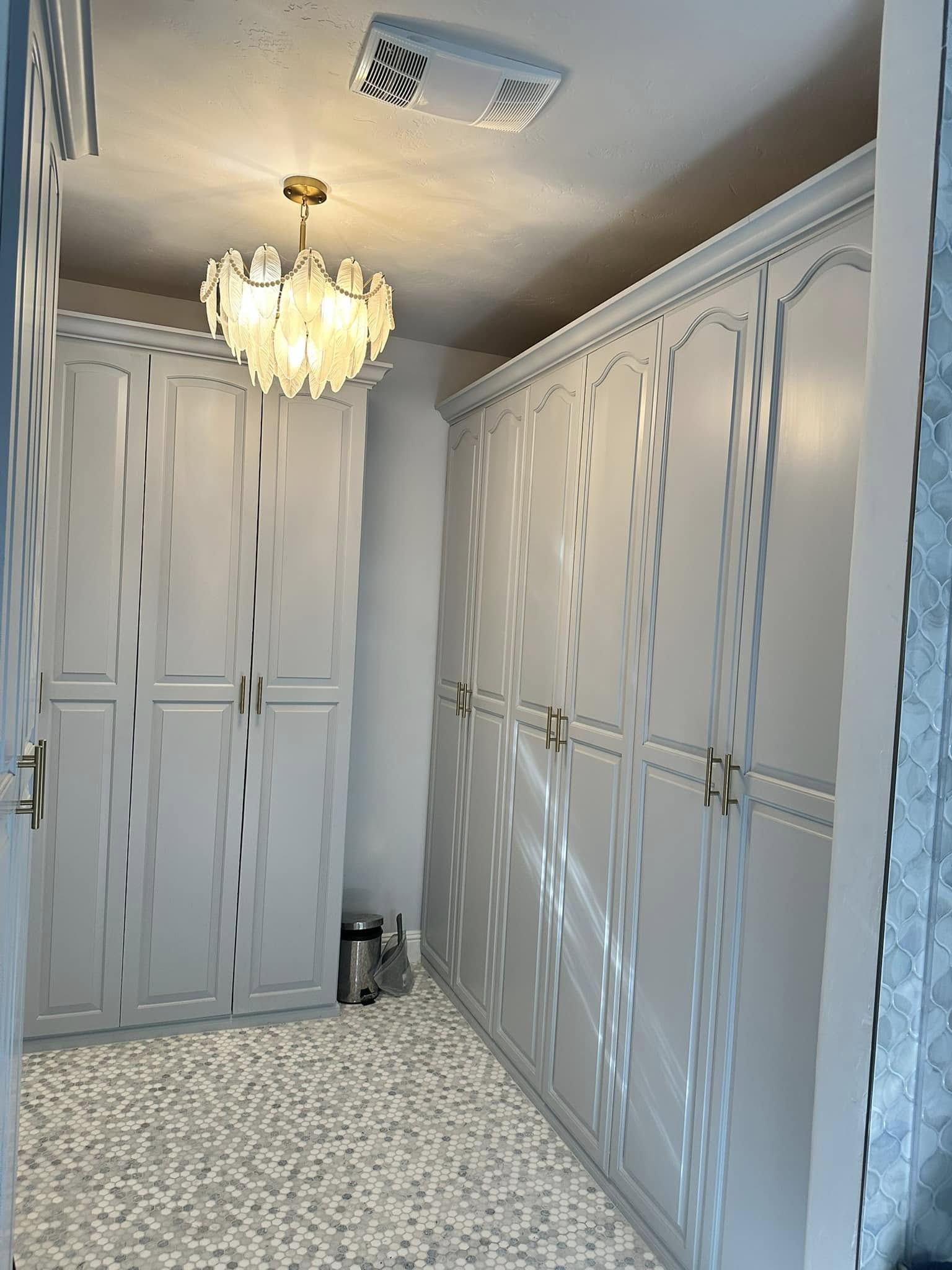 Luxurious walk-in closet with white cabinetry, brass chandelier, and marble hexagon tile flooring